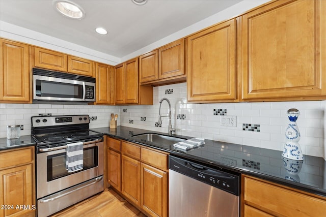 kitchen with appliances with stainless steel finishes, backsplash, sink, and light hardwood / wood-style flooring