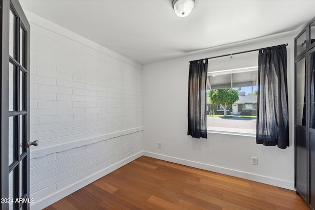 empty room with brick wall and hardwood / wood-style floors