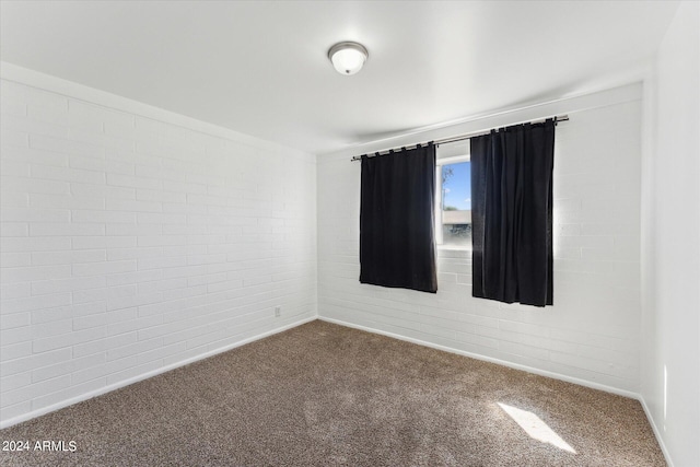 carpeted empty room featuring brick wall