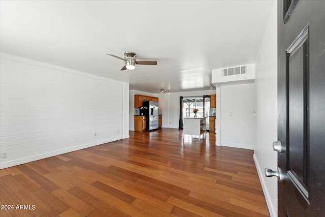 unfurnished living room with ceiling fan, brick wall, and dark wood-type flooring