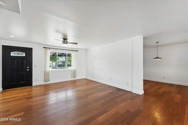 unfurnished living room featuring ceiling fan, brick wall, and dark hardwood / wood-style flooring