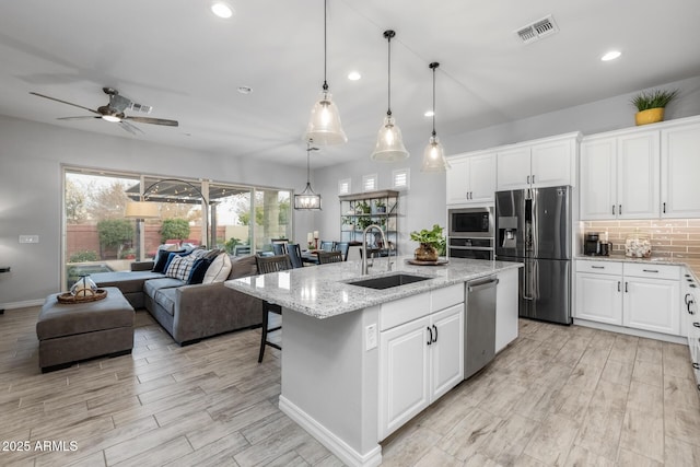 kitchen featuring white cabinets, stainless steel appliances, a kitchen island with sink, and sink