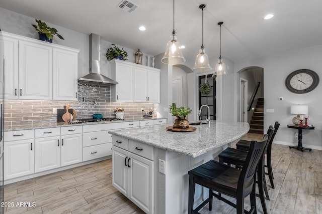 kitchen featuring a kitchen bar, wall chimney exhaust hood, a kitchen island with sink, sink, and white cabinets