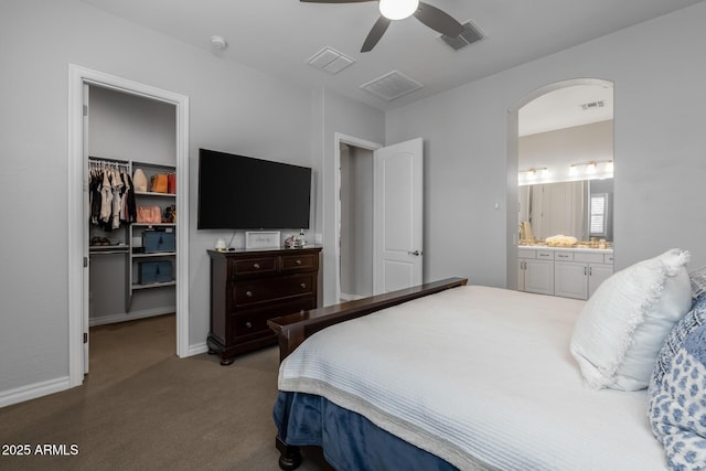 bedroom featuring light carpet, ceiling fan, a spacious closet, connected bathroom, and a closet