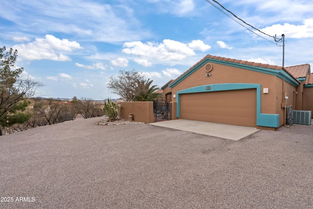 garage featuring gravel driveway, a gate, central AC unit, and fence