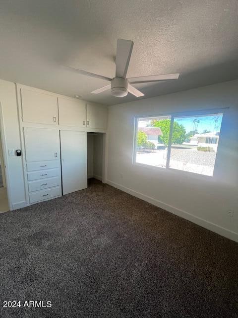 unfurnished bedroom featuring ceiling fan, a textured ceiling, a closet, and carpet