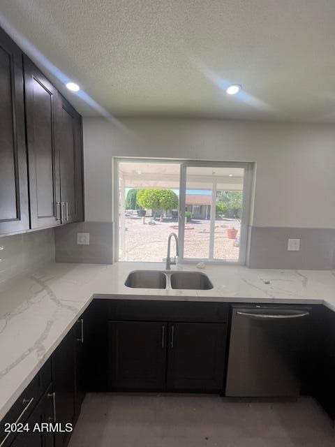 kitchen featuring light stone countertops, dark brown cabinetry, sink, and stainless steel dishwasher