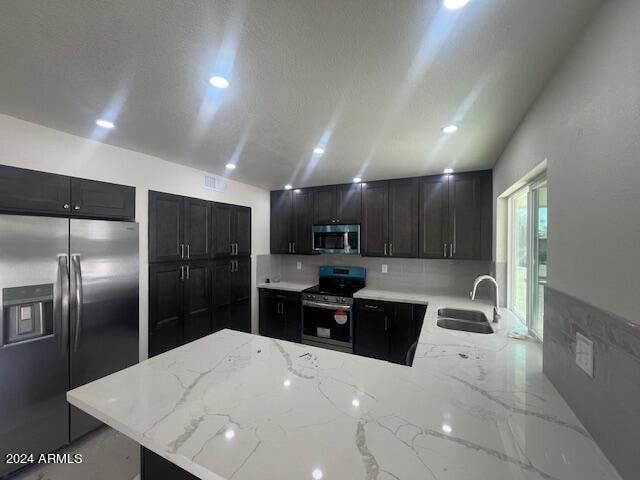 kitchen with appliances with stainless steel finishes, kitchen peninsula, light stone countertops, and sink