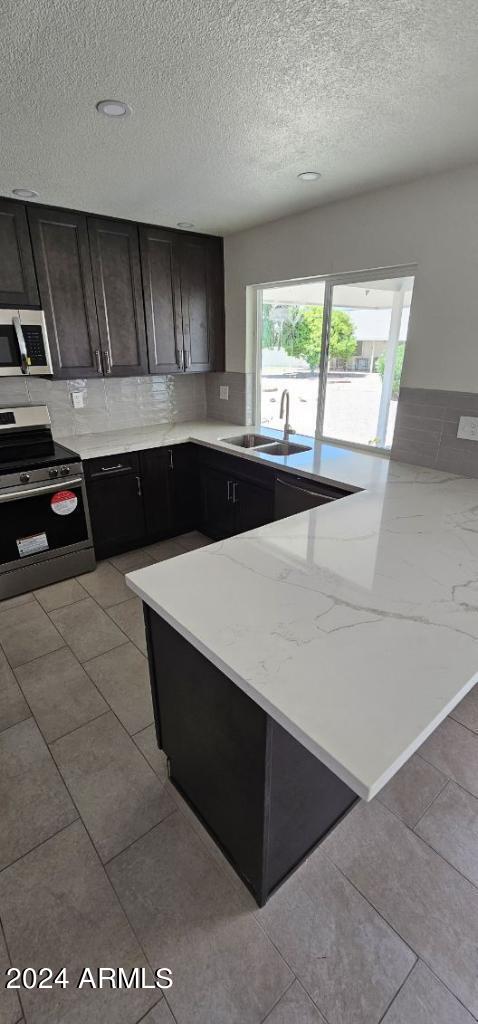 kitchen featuring dark brown cabinetry, a textured ceiling, appliances with stainless steel finishes, and sink