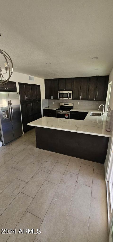 kitchen with sink, kitchen peninsula, pendant lighting, appliances with stainless steel finishes, and dark brown cabinets