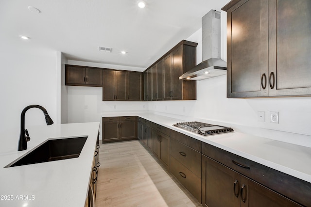 5875 N 193rd Dr, Litchfield Park, AZ 85340 - kitchen featuring dark brown cabinets, wall chimney range hood, stainless steel gas cooktop, light wood-style flooring, and a sink