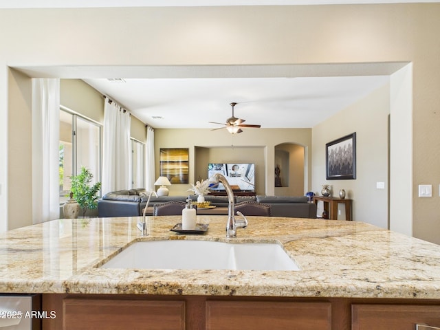 kitchen featuring brown cabinetry, light stone countertops, open floor plan, and a sink