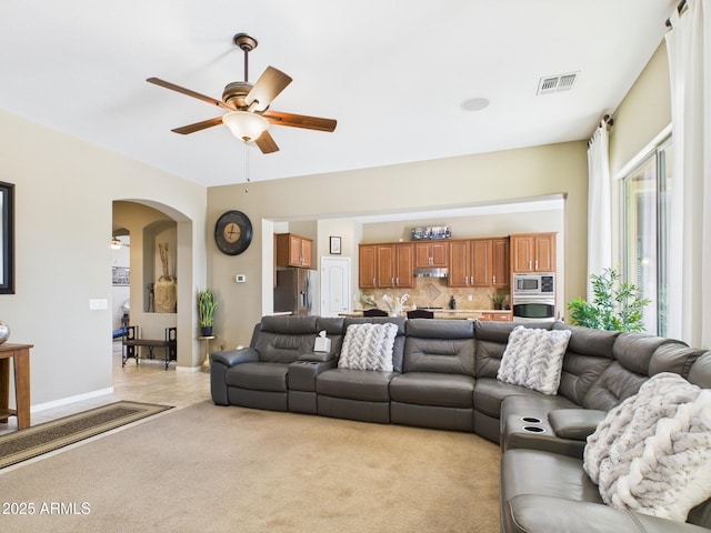 living room featuring visible vents, light carpet, arched walkways, baseboards, and ceiling fan