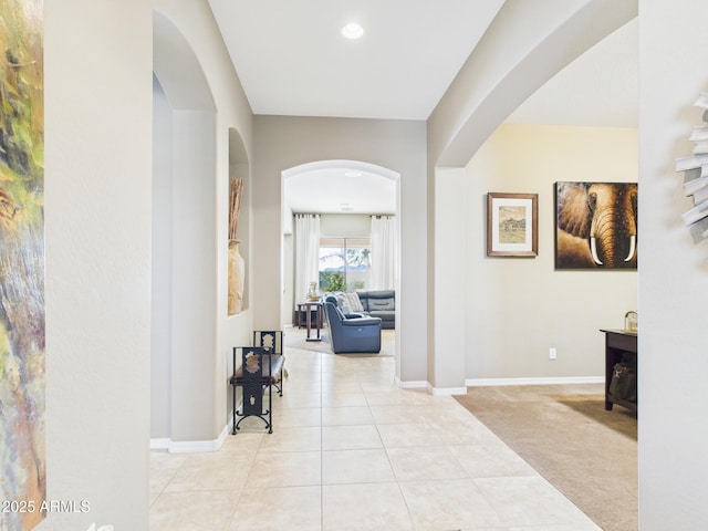 hall featuring arched walkways, tile patterned flooring, carpet flooring, and baseboards