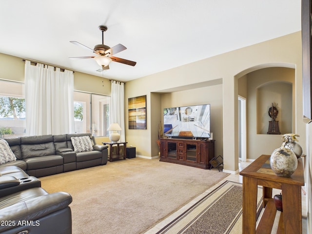 carpeted living room featuring arched walkways, baseboards, and ceiling fan