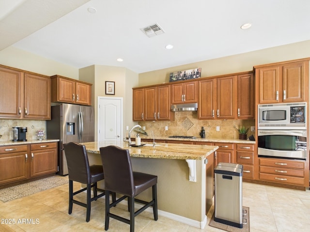 kitchen featuring visible vents, under cabinet range hood, a kitchen bar, stainless steel appliances, and a sink