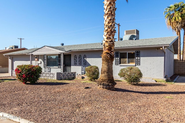 ranch-style home with an attached garage, a shingled roof, cooling unit, and brick siding