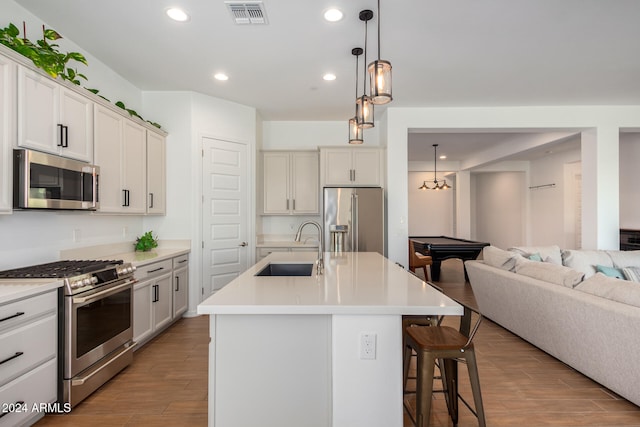 kitchen with an island with sink, sink, light wood-type flooring, and high end appliances