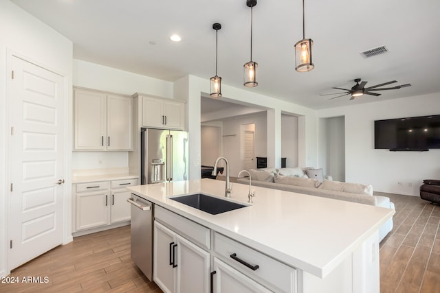 kitchen with a kitchen island with sink, sink, hanging light fixtures, light hardwood / wood-style flooring, and appliances with stainless steel finishes