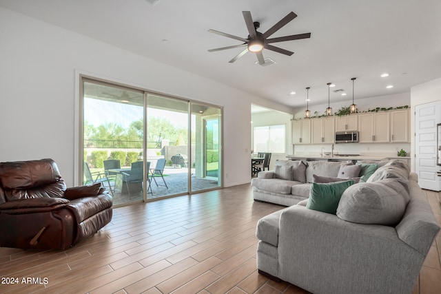 living room with light wood-type flooring, ceiling fan, and sink