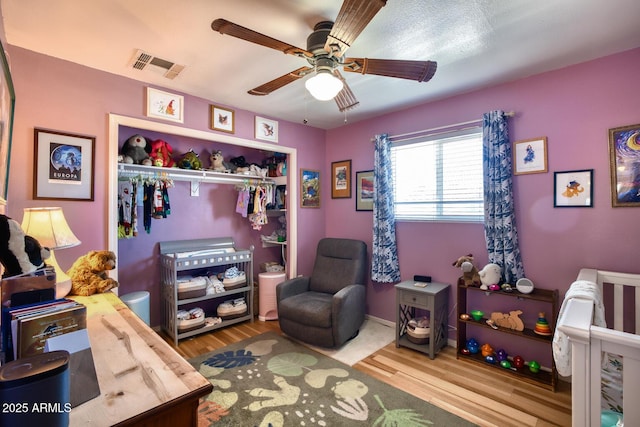 bedroom featuring ceiling fan, a closet, wood finished floors, and visible vents