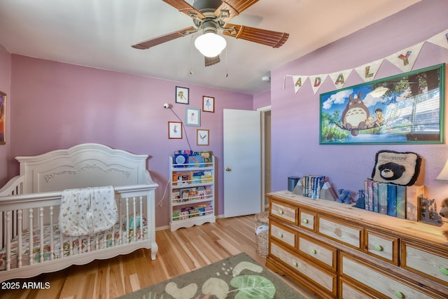 bedroom with baseboards, ceiling fan, wood finished floors, and a nursery area