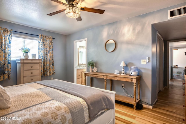 bedroom featuring visible vents, light wood-style floors, baseboards, a ceiling fan, and ensuite bath