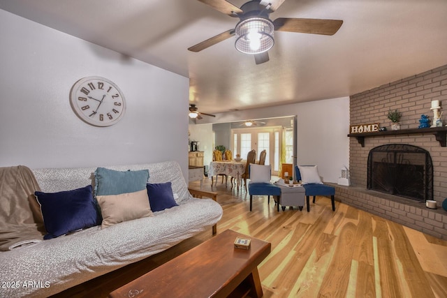 living area featuring a brick fireplace, ceiling fan, and wood finished floors