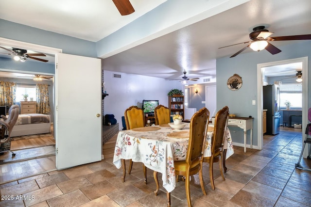 dining room with ceiling fan, visible vents, plenty of natural light, and stone tile flooring