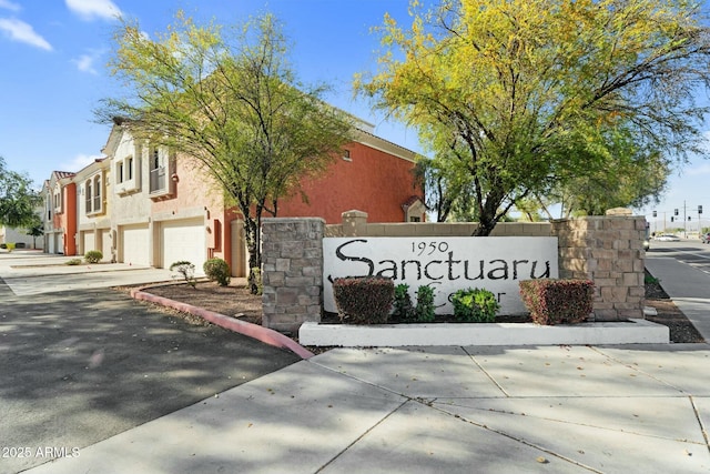 community sign with concrete driveway and an attached garage