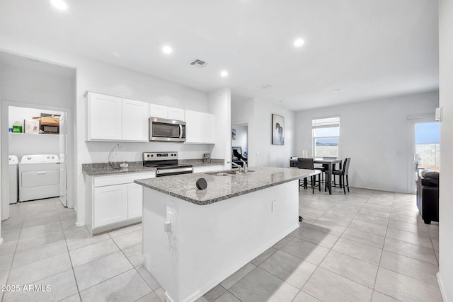 kitchen with white cabinets, appliances with stainless steel finishes, a kitchen island with sink, and washing machine and clothes dryer