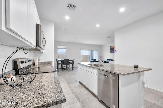 kitchen featuring appliances with stainless steel finishes, sink, stone counters, white cabinets, and an island with sink