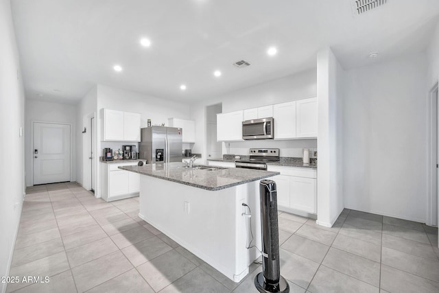 kitchen with appliances with stainless steel finishes, dark stone counters, a kitchen island with sink, sink, and white cabinetry