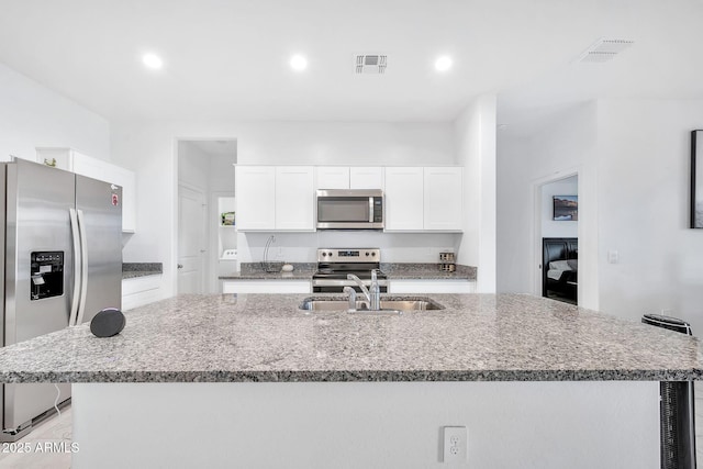 kitchen featuring a center island with sink, light stone counters, white cabinets, and stainless steel appliances