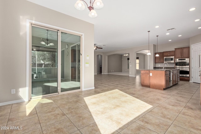 kitchen with pendant lighting, a kitchen island with sink, light tile patterned floors, ceiling fan with notable chandelier, and appliances with stainless steel finishes