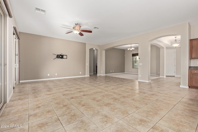 tiled empty room with ceiling fan with notable chandelier