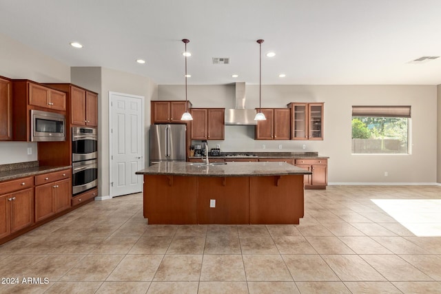 kitchen featuring a center island with sink, wall chimney exhaust hood, appliances with stainless steel finishes, decorative light fixtures, and a breakfast bar area