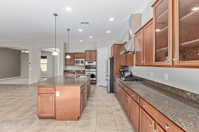 kitchen with stainless steel appliances, sink, dark stone countertops, hanging light fixtures, and an island with sink