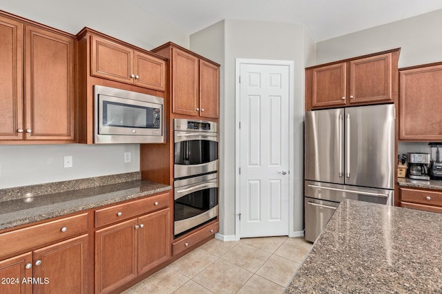 kitchen with stainless steel appliances, dark stone counters, and light tile patterned flooring