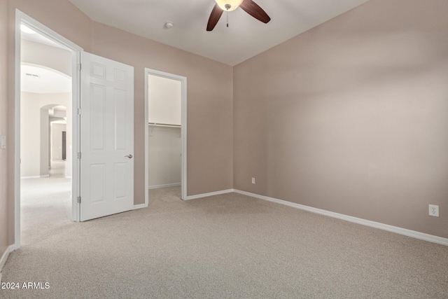 unfurnished bedroom featuring light carpet, a walk in closet, a closet, and ceiling fan