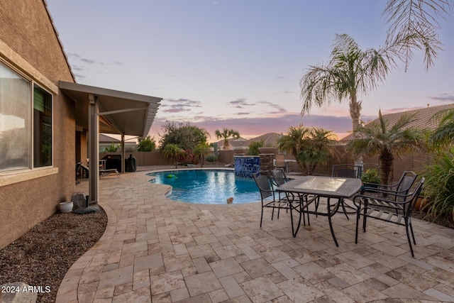 pool at dusk with pool water feature and a patio area