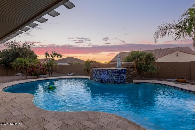 pool at dusk featuring pool water feature and a patio