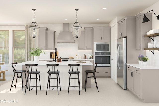 kitchen featuring gray cabinetry, appliances with stainless steel finishes, hanging light fixtures, and wall chimney range hood