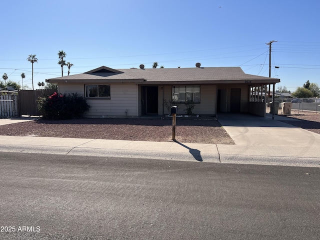 ranch-style house featuring driveway, fence, an attached carport, and roof with shingles