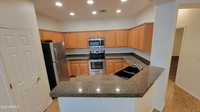 kitchen featuring visible vents, appliances with stainless steel finishes, a sink, dark stone countertops, and a peninsula