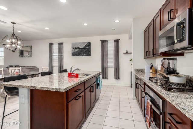 kitchen featuring stainless steel appliances, a sink, light tile patterned flooring, a chandelier, and a breakfast bar