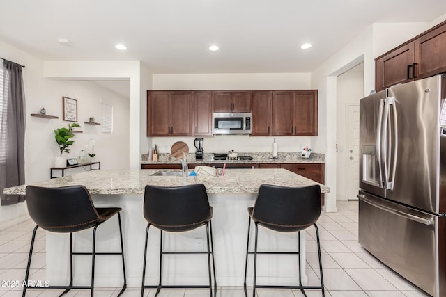 kitchen with stainless steel appliances, light tile patterned flooring, a breakfast bar, a kitchen island with sink, and recessed lighting