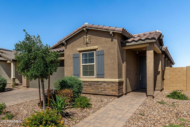 view of front of house featuring stucco siding, a tile roof, fence, an attached garage, and stone siding
