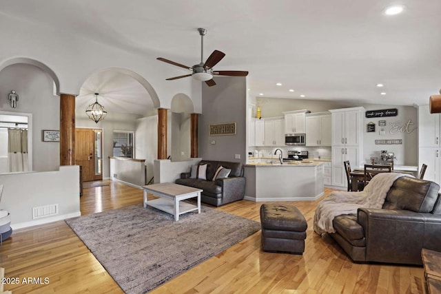 living room featuring lofted ceiling, sink, ceiling fan with notable chandelier, and light hardwood / wood-style flooring