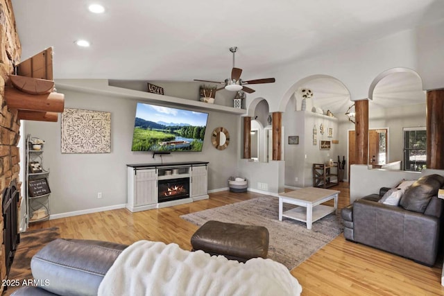 living room with vaulted ceiling, ceiling fan, a stone fireplace, and light wood-type flooring